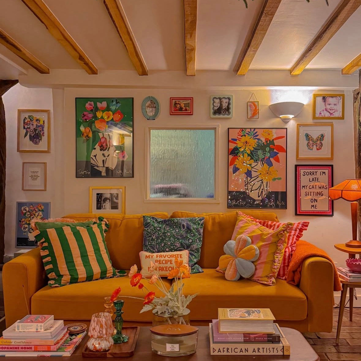 Living room with a yellow couch, colorful pillows, and various artworks on the walls.