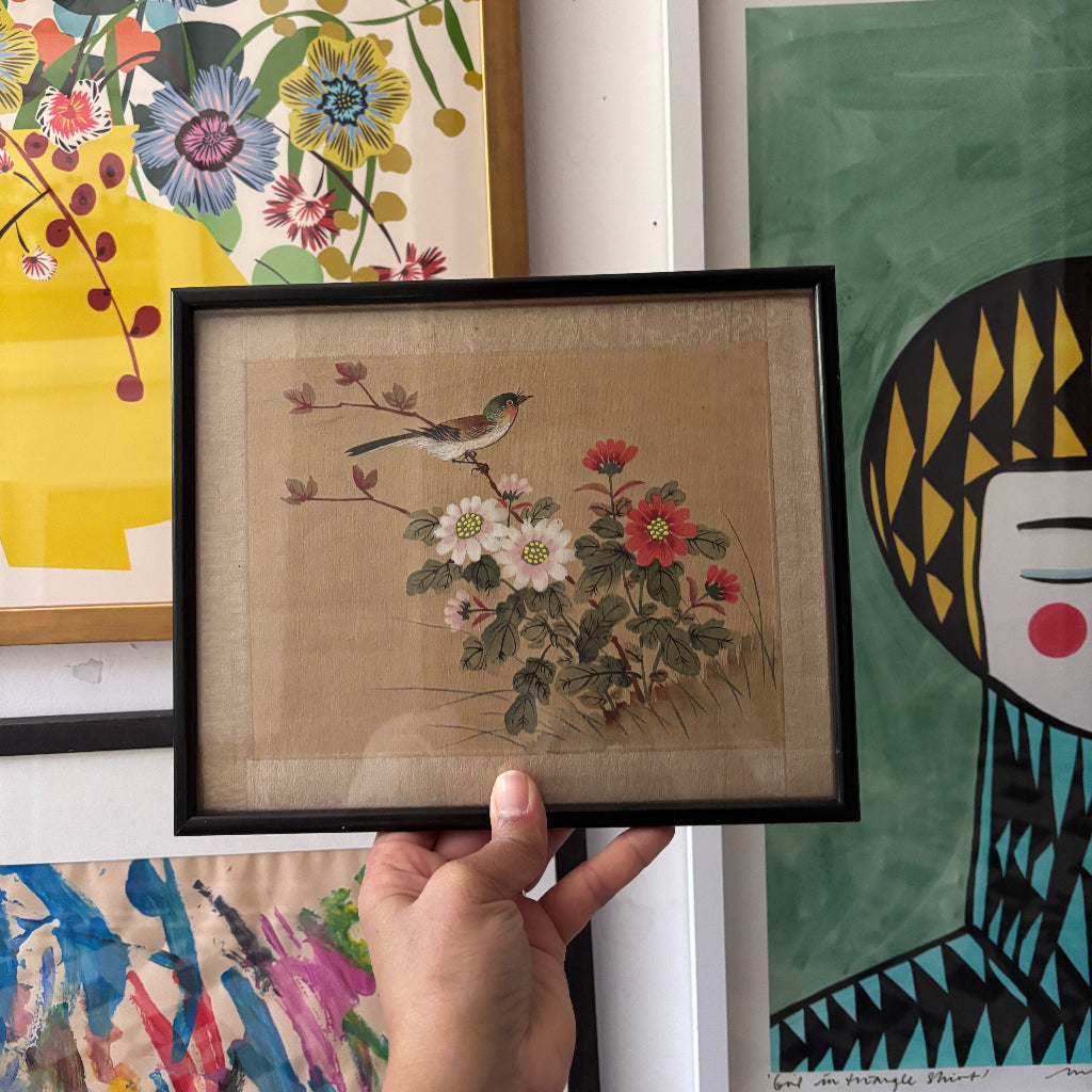 Framed artwork of a bird and flowers held in front of colorful wall art