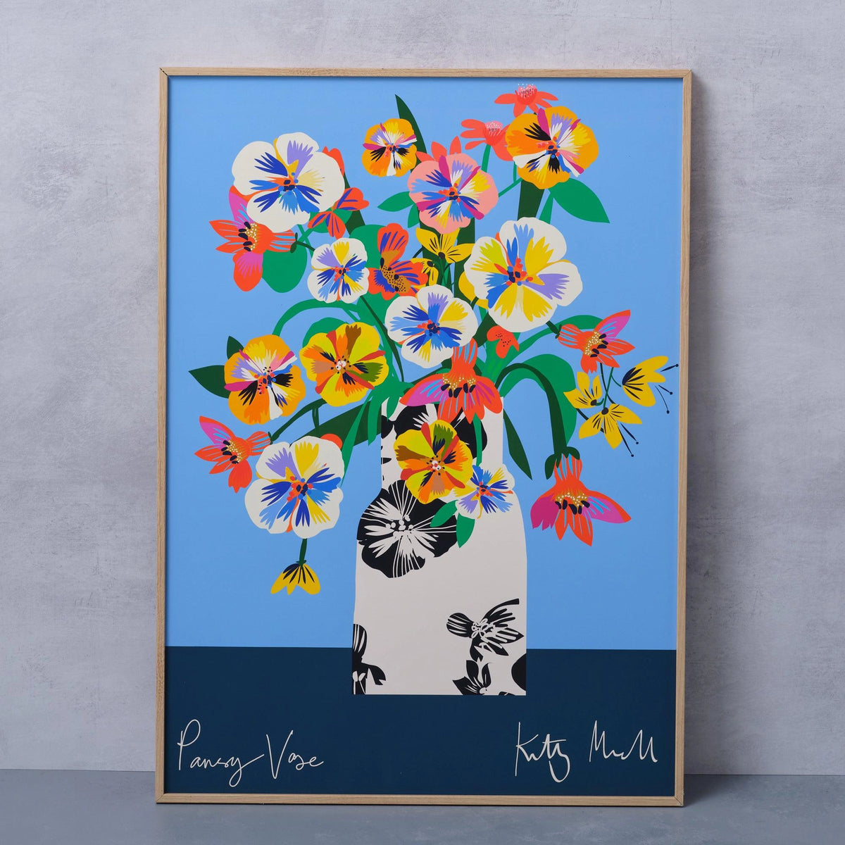 Pansy Vase fine art print by Kitty McCall in a natural oak frame, leaning against a concrete wall