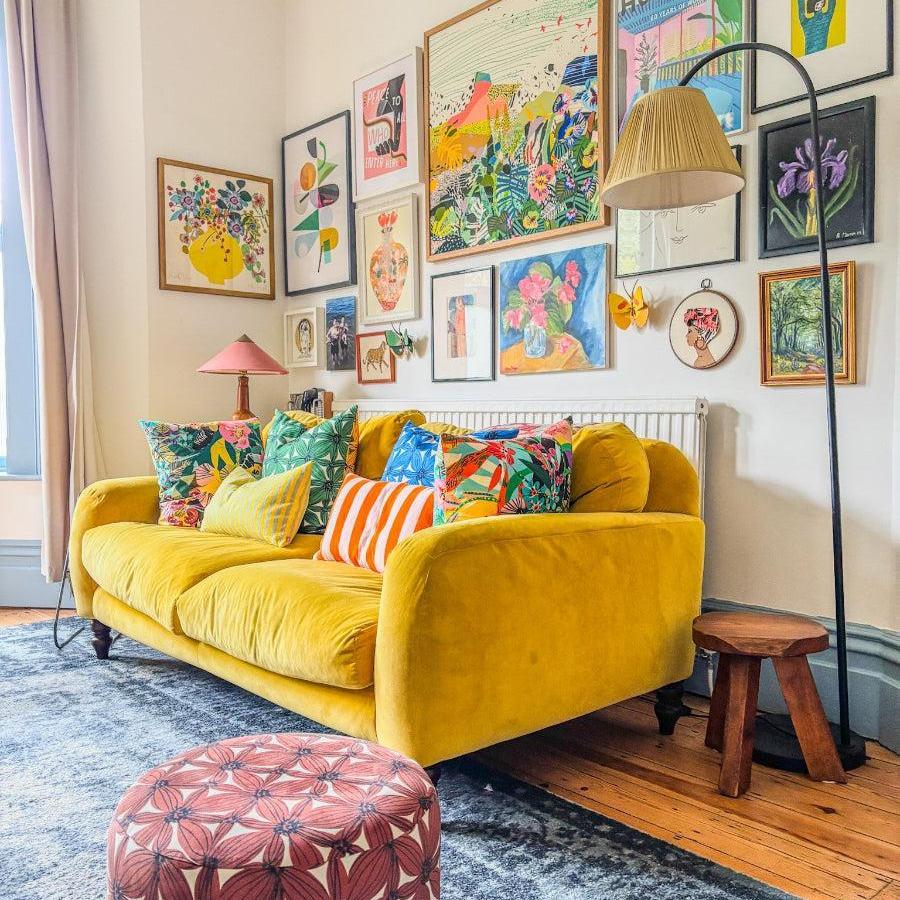 Living room with a yellow sofa, colorful pillows, and a wall of framed artwork.