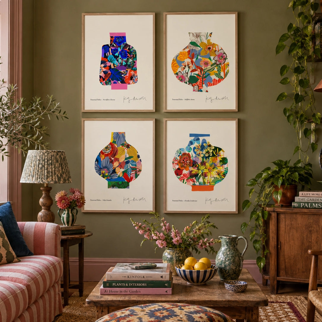 A styled living room featuring a set of four framed art prints depicting colorful abstract vase illustrations on a sage green wall. The room includes a pink-and-white striped sofa, a wooden coffee table with books and fruit, and various potted plants.