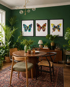 Dining room with a round wooden table, chairs, and butterfly artwork on a green wall.