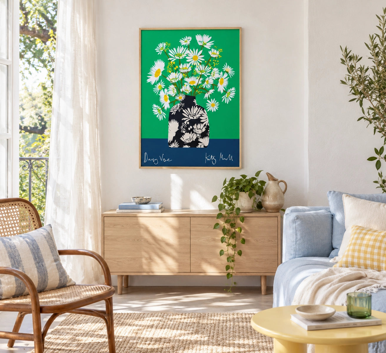 Daisy Vase fine art print by Kitty McCall in a natural oak frame, hung above a light oak sideboard in a bright, airy living room with rattan chair, blue sofa and trailing houseplant