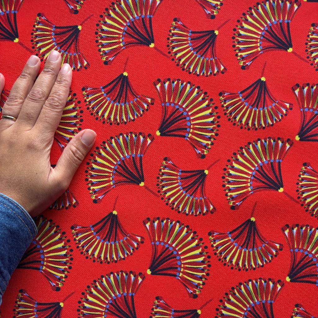 Hand touching a fabric with a red and gold pattern