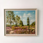 Framed painting of a landscape with trees and open field on a white wall