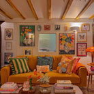 Living room with a yellow couch, colorful pillows, and various artworks on the walls.