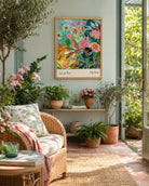 Jardin de Fleurs fine art print by Kitty McCall in a natural oak frame, hung in a sunny garden room styled with a wicker chair, terracotta pots, pink flowers and an olive tree