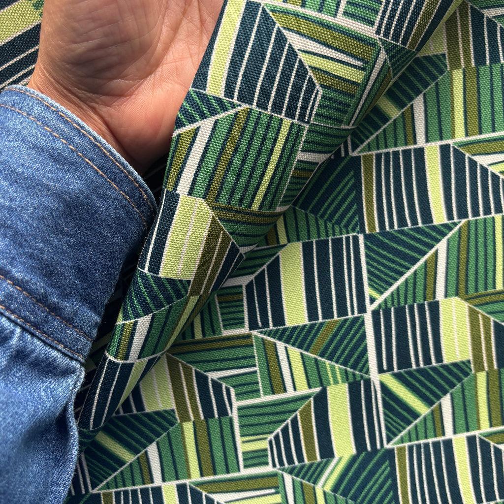 Close-up of green and blue geometric patterned fabric held by a person wearing blue jeans.
