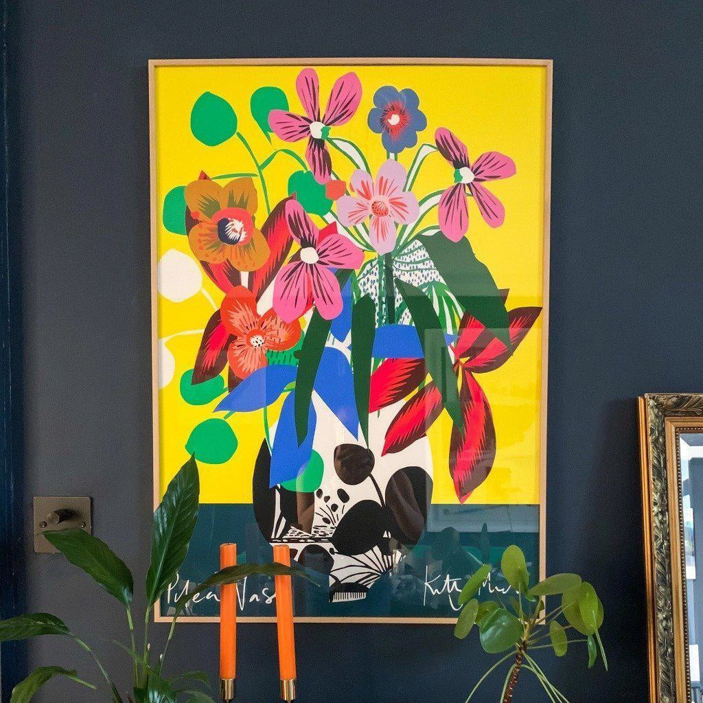 Pilea Vase fine art print by Kitty McCall in a natural oak frame displayed on a dark navy wall with houseplants and orange candles