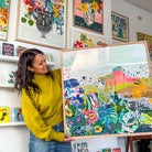 Catherine Nice holding an 80×80 cm Flowers of Utopia fine art print in a natural oak frame in her studio