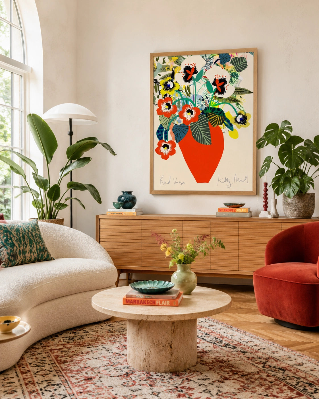 Red Vase fine art print by Kitty McCall in a natural oak frame, hung above an oak sideboard in a bright living room with arched window, boucle sofa, terracotta armchair and large tropical houseplants